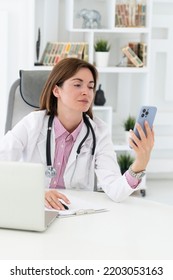 Close Up Portrait Of Tired Female Doctor Sitting At The Desktop And Talking To Phone In The Office Of Modern Clinic	