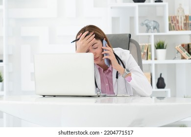 Close Up Portrait Of Tired Female Doctor Sitting At The Desktop And Talking To Phone In The Office Of Modern Clinic