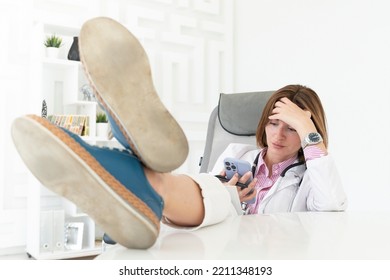 Close Up Portrait Of Tired Female Doctor Sitting At The Desktop And Talking To Phone In The Office Of Modern Clinic