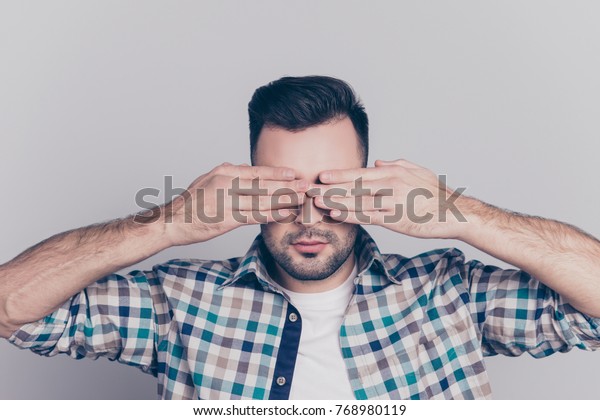 Close up portrait of tired man with stubble\
after long working day on computer having eye problem, pressure,\
covering face, eyes with hands, afraid to look, standing over grey\
background