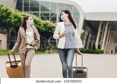 Close Up Portrait Of Two Business Women In Protective Masks With Suitcases Near The Airport. Young Women Near Airport, Opening Air Travel, Travel Concept. Business Trips During Coronavirus Quarantine