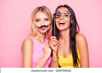 Close up portrait of two crazy funny cheerful comic attractive beautiful girlfriends wearing summer clothes and having fun using fake mustache and eyewear, isolated on bright pink background
