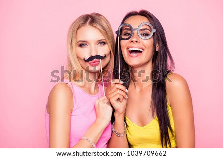 Close up portrait of two crazy funny cheerful comic attractive beautiful girlfriends wearing summer clothes and having fun using fake mustache and eyewear, isolated on bright pink background