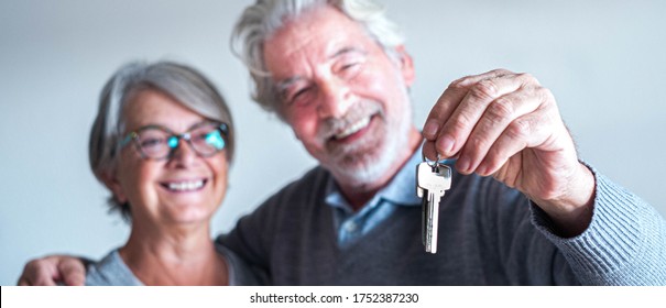 close up and portrait of two seniors or mature people buying a new house or car or some property - independent lifesyle and concept - pensioner man holding two keys in his hand with his wife looking