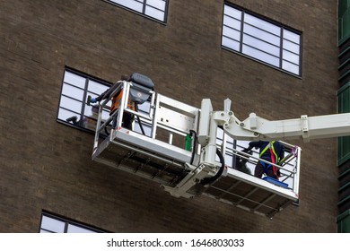 A close up portrait of two window washers, using a crane to get to the top windows of the building in a big box to do their cleaning job in comfort.
