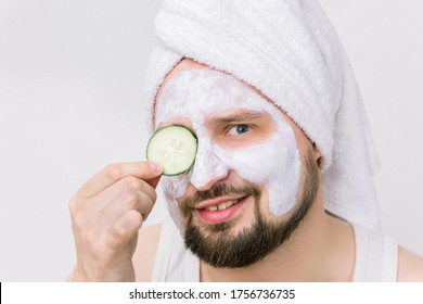 Close Up Portrait Of Unshaven Bearded Man In White Towel Oh His Head, Having Cosmetic Mask After Shower, Posing With Slice Of Cucumber Covering His Eye