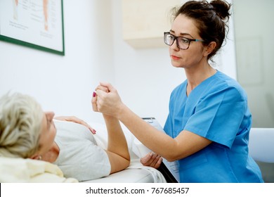 Close Up Portrait View Of Middle Aged Professional Nurse Holding Hands With A Patient While Woman Patient Lying On The Bed In Front.