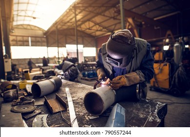 Close up portrait view of professional mask protected welder man working on the metal sculpture in the industrial fabric workshop in front of few other workers. - Powered by Shutterstock