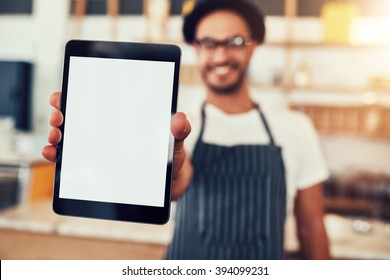Close Up Portrait Of A Waiter Holding Up A Tablet Computer With A Empty Display. Coffee Shop Owner Showing A Digital Tablet.