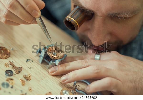 Close up portrait of a watchmaker at\
work.Old pocket watch being repaired by watch\
maker.