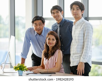 Close Up And Portrait Wealthy Successful Asian Business Family Looking At Camera, Smiling Confidently, Proudly And Happy While Sitting, Working And Using Computer In Comfortable Office During The Day