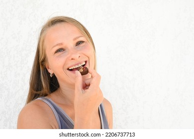 Close Up Portrait Of Woman Biting A Chocolate Candy On Light Backround. Happy 35 Years Old Woman Eating Chocolate.