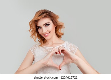 Close Up Portrait Of Woman Giving Showing Heart Shape Figure, Love Symbol With Fingers, Pretty, Charming, Nice, Attractive Woman With Beaming Smile With Curly Hair Isolated White Light Grey Background