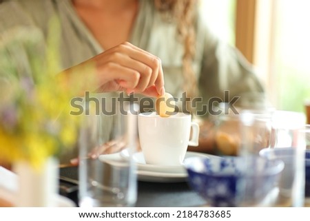 Close up portrait of a woman hand dipping cookie in milk in a restaurant