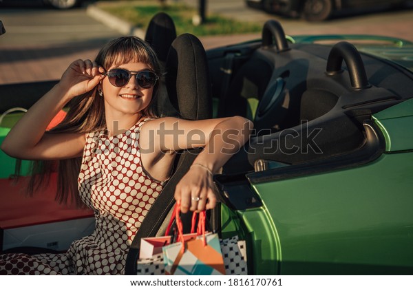 Close up portrait of woman sitting in\
the cabriolet car with shopping bags and\
smiling.