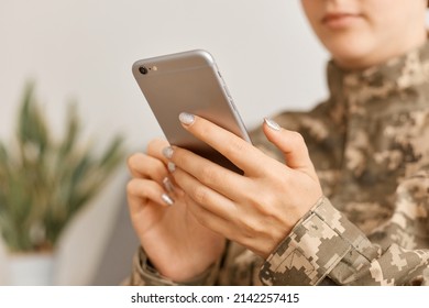 Close up portrait of woman soldier wearing camouflage uniform sitting with smart phone in hands, using cell phone, checking social network or work chat. - Powered by Shutterstock