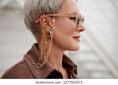 Close up portrait of woman wearing fashion accessories and jewelry, glasses on gold chain, earrings and clips, side view - Shutterstock ID 2277023571