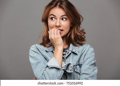 Close up portrait of a worried teenage girl in denim jacket biting her nails and looking away isolated over gray background - Shutterstock ID 751016992