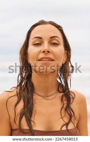 Close up portrait young adorable wet hair suntanned woman is looking to camera, standing and relaxing, enjoing of weather, breathing with moisture on the sand beach at the wind in Thailand
