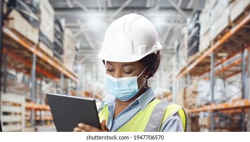 Close Up Portrait Of Young African American Woman Engineer In Medical Mask Typing On Tablet Standing At Construction Site. Female Builder In Helmet Working Tapping On Device At Factory. Work Concept