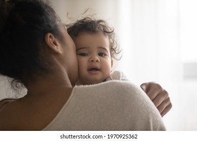 Close Up Portrait Of Young African American Mother Hold In Arms Hug Cuddle Little Ethnic Baby Girl Child. Biracial Mom Embrace Caress Lull And Kiss Small Toddler Daughter Kid. Motherhood Concept.