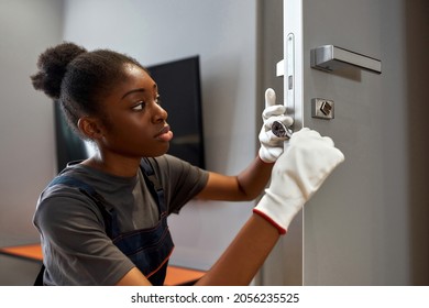 Close portrait of young African American woman in white gloves fixing door lock, using professional tools. Skilled woman troubleshooting lock in appartment's door. - Powered by Shutterstock