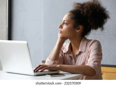 Close up portrait of a young african american woman looking out window when working on laptop