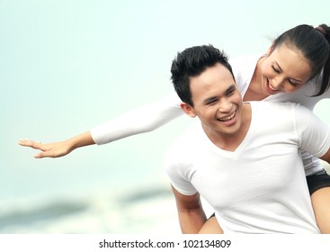 Close Up Portrait Of A Young Asian Man Giving Piggyback To Woman On The Beach.