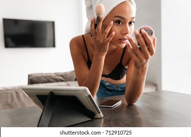 Close Up Portrait Of A Young Asian Woman With Bath Towel On Head Doing Her Make Up While Leaning On A Table And Looking At The Mirror