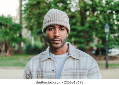 Close up portrait of young attractive african american man with beanie hat looking serious at camera. Front view of a hispanic guy standing in a park outdoors with sad attitude. High quality photo - Powered by Shutterstock