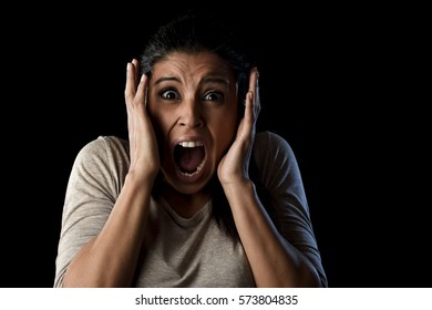 close up portrait young attractive Latin woman desperate and scared isolated on black background looking terrorized and horrified screaming in primal fear emotion face expression
