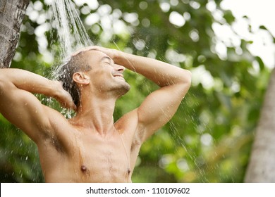 Close up portrait of a young attractive man having a shower in a tropical garden with palm trees while on vacations, smiling. - Powered by Shutterstock