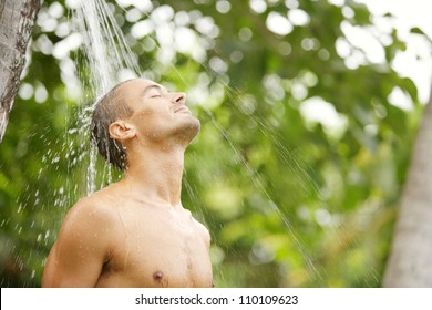 Close up portrait of a young attractive man having a shower in a tropical garden with palm trees while on vacations. - Powered by Shutterstock