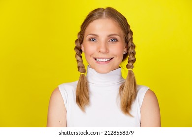 Close up portrait of young attractive smiling girl with pigtails standing isolated over yellow background
