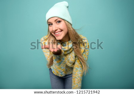 Close up portrait of young attractive woman with blonde straight hair, knitted hat, wearing stylish clothes, have a perfect makeup. Turquoise background