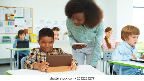 Close up portrait of young beautiful African American woman teacher helping little schoolboy at lesson, elementary school education, computer science class. Junior student tapping on tablet at lesson