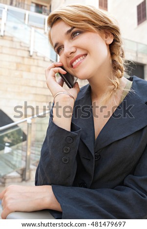 Close up portrait of young beautiful business woman using smart phone in financial city, speaking phone call conversation, outdoors. Professional using technology, smiling. Lifestyle exterior.