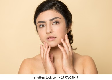 Close up portrait of young beautiful Indian woman isolated on yellow studio background touch healthy glowing skin after facial salon treatment. Millennial mixed race female after skincare procedures.
