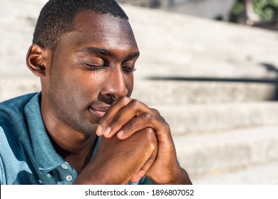 Close up portrait young black man with eyes closed praying outside