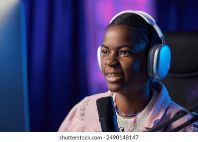 Close up portrait of young Black woman wearing headphones and speaking to microphone while streaming video games or recording podcast copy space - Powered by Shutterstock