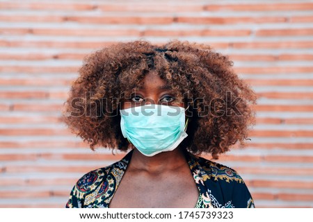 Close up portrait of young black woman wearing face medical mask to prevent coronavirus infection. bricks background. Protection against viruses