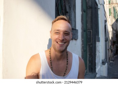 Close Up Portrait Of A Young Blonde Man Smiling Against A Wall In Italy