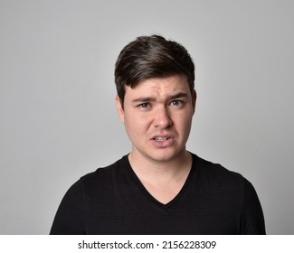 close up portrait of young brunette man, head and shoulders wearing basic black shirt, with expressive dramatic facial expressions, isolated on studio background. - Shutterstock ID 2156228309