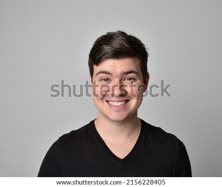 close up portrait of young brunette man, head and shoulders wearing basic black shirt, with expressive dramatic facial expressions, isolated on studio background.