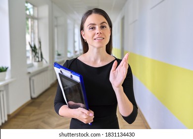 Close Up Portrait Of Young Business Woman Talking And Gesturing Looking At Camera Inside Office Building. Head Shot Of Female Teacher, Psychologist, Social Worker In School Corridor