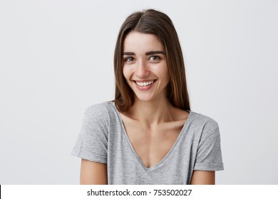 Close up portrait of young cheerful beautiful girl with dark long hair in casual gray shirt smiling with teeth, looking in camera with happy and relaxed face expression, posing for university photo.