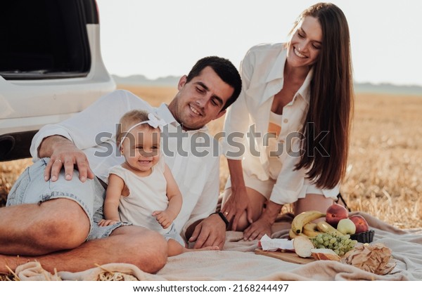 Close Up Portrait of Young Family, Mother and Father\
with Their Toddler Daughter Having Picnic Time Outdoors During\
Their Road Trip with Car