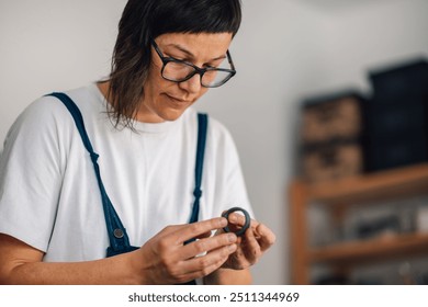 Close up portrait of young female creative and talented pottery designer standing at ceramics workshop and making clay circle. Focused female potter in overalls making cup holder at pottery studio. - Powered by Shutterstock