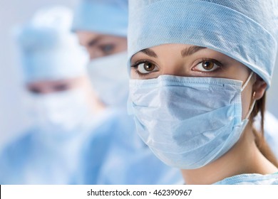 Close Up Portrait Of Young Female Surgeon Doctor Surrounded By Her Team. Group Of Surgeon In Operation Theatre. Healthcare, Medical Education, Emergency Medical Service And Surgery Concept