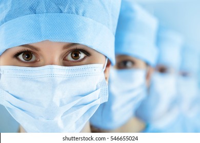 Close Up Portrait Of Young Female Surgeon Doctor Surrounded By Her Team. Group Of Surgeon In Operation Theatre. Healthcare, Medical Education, Emergency Medical Service And Surgery Concept